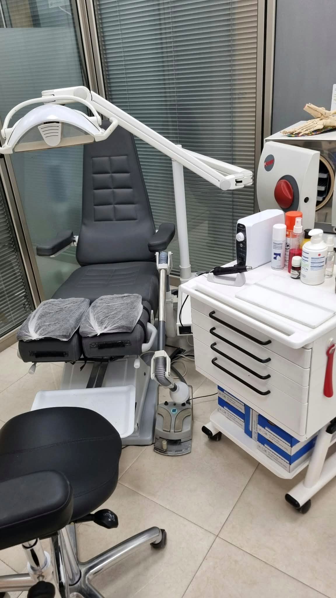 Sillón de podología con lámpara y carro de instrumental en la consulta